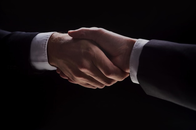 Photo of two men in suits shaking hands on a black background