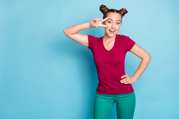 Photo of white cheerful cute positive nice pretty girlfriend smiling toothily wearing pants trousers with hand on waist showing v-sign isolated pastel blue color wall 