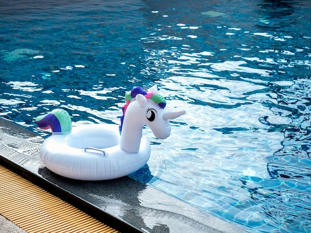 Photo of the white inflatable ring cute unicorn doll in the outdoor swimming pool with copy space Empty swim ring for children with sunshine for summer beach