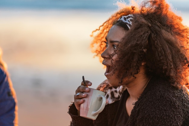 Photo with copy space of a surprised latin woman drinking tea during sunset on a beach