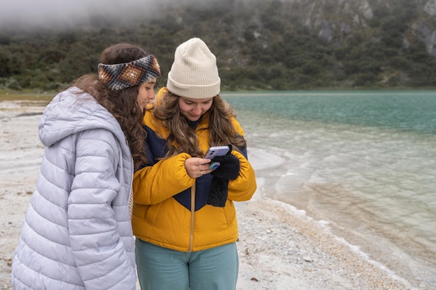 Photo with copy space of two girls using a mobile next to a lagoon in a glacier