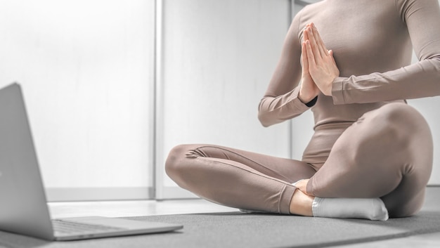 Photo of woman practicing yoga training online at home with laptop.