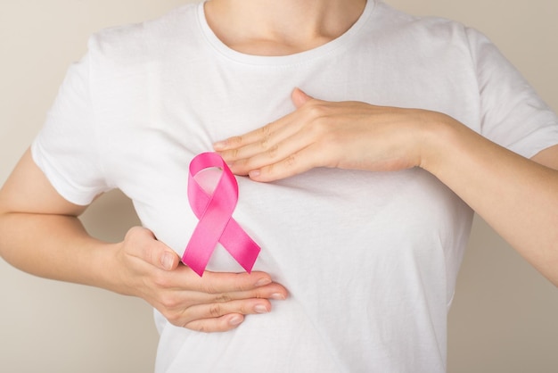 Photo of woman in white tshirt with pink ribbon self examining her breasts on isolated grey background