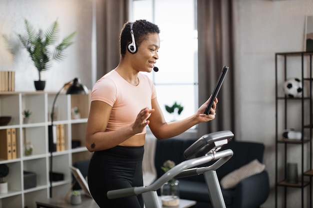 Photo of young active african business woman in sportswear and headset training at home