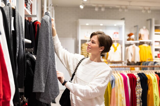 Photo of young attractive brunette woman with a short haircut in a white sweater chooses stylish and