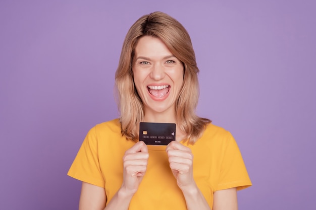 Photo of young attractive excited woman happy positive smile credit card money income isolated on violet color background