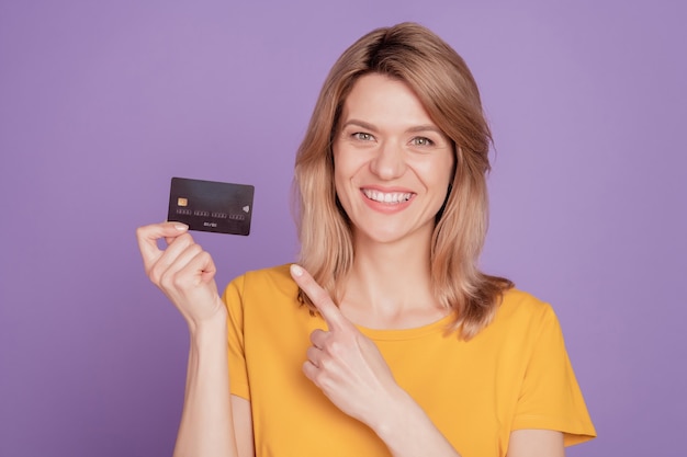 Photo of young attractive woman happy positive smile point finger credit card ad advice isolated on violet color background