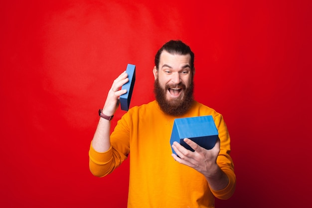 Photo of young bearded man in yellow sweater looking amazed at his gift