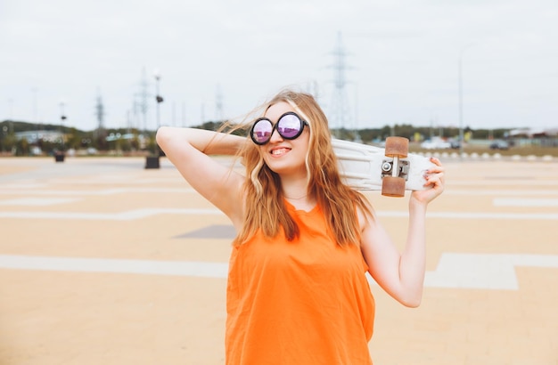 Photo of a young beautiful girl walking outdoors with a skateboard teenager generation z