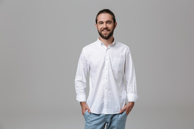 Photo of a young cheerful happy optimistic positive handsome bearded man posing isolated over grey wall.