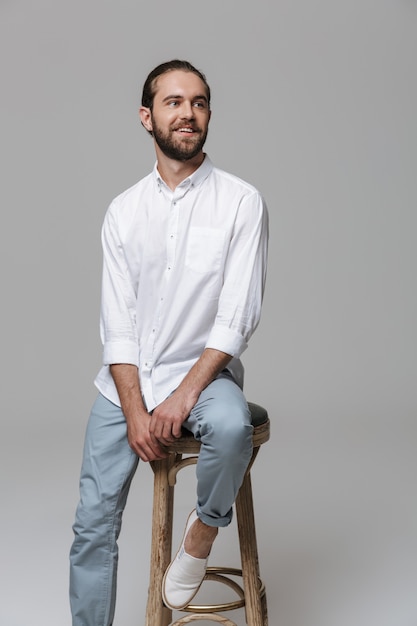 Photo of a young cheerful happy optimistic positive handsome bearded man posing isolated over grey wall.