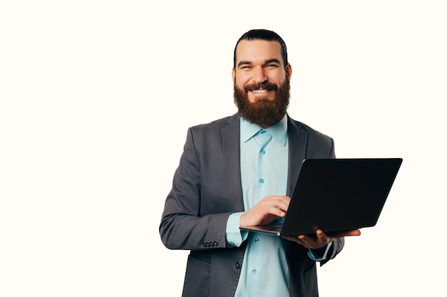 Photo of young cheerful man in casual suit holding laptop and looking at the camera