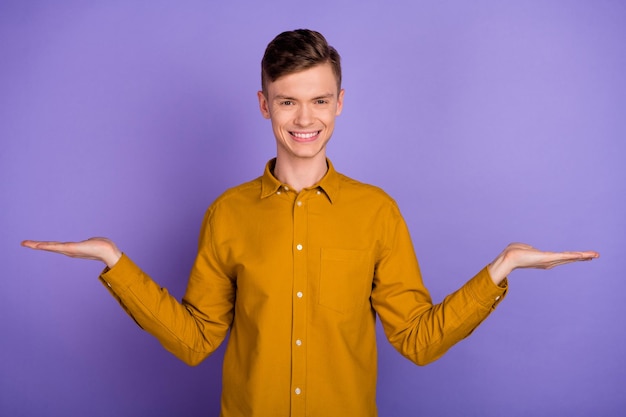 Photo of young cheerful man hold hands proposition scales advertise isolated over violet color background