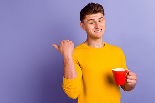 Photo of young cheerful man indicate finger empty space promo latte isolated over violet color background