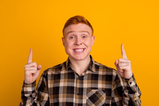 Photo of young cheerful man indicate fingers empty space promo recommend isolated over yellow color background