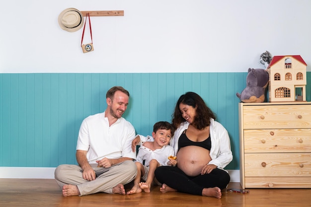 Photo of young cheerful positive smiling couple pregnant wife and husband with their son relaxing at home