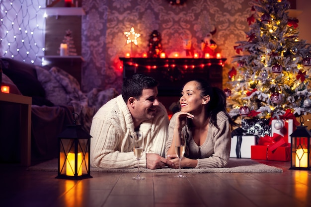 Photo of young couple resting by the fireplaec in the christmas room. Celebrating christmas. Christmas tree.