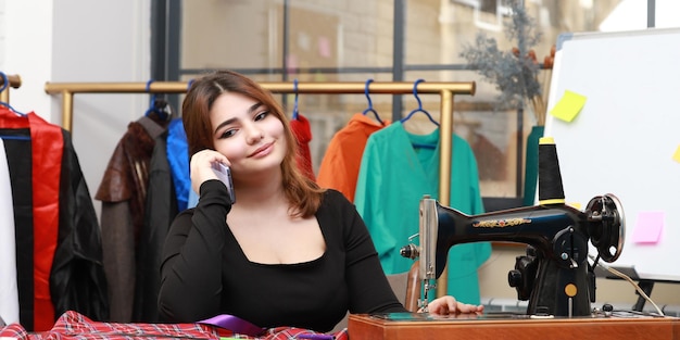 Photo of young female tailor talking on the phone at the atelier