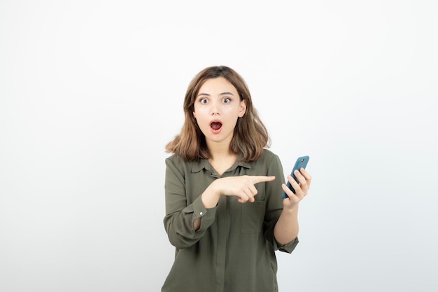 Photo of young girl with cellphone standing over white wall. High quality photo