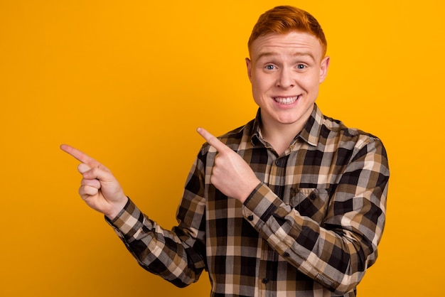 Photo of young guy indicate fingers empty space ads promo banner isolated over yellow color background