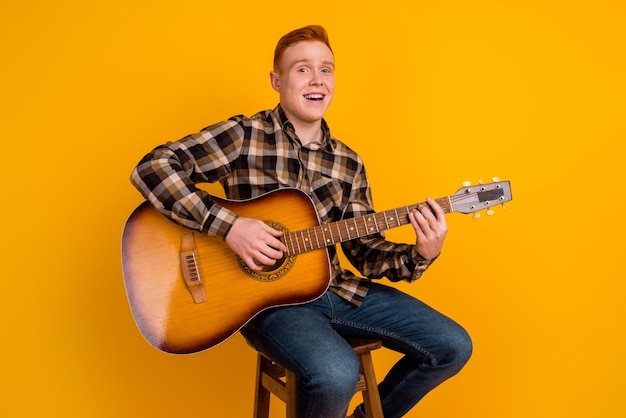 Photo of young handsome man sit chair play guitar concert music song isolated over yellow color background