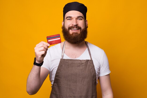 Photo of young happy Chef showing red credit card while standing over 