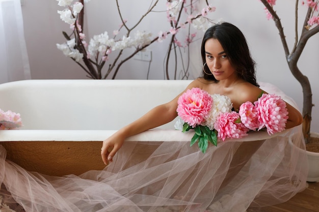 Photo of young hot model sitting in a bathtub and holding bunch of flowers High quality photo