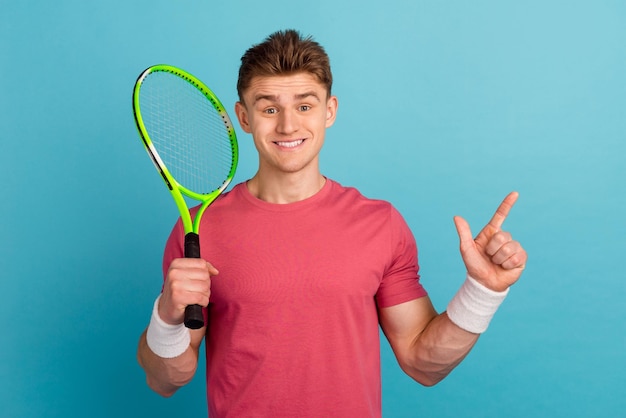 Photo of young man hold racket game indicate finger empty space recommend isolated over blue color background