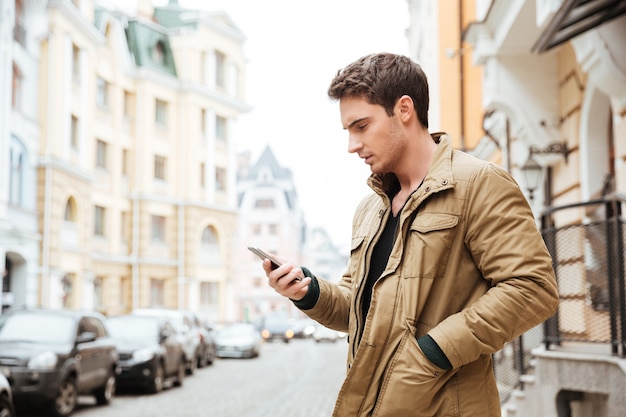 Photo of young man walking on the street and chatting by his phone outdoors. Look at phone.