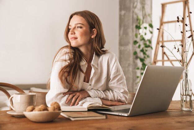 Photo of young pretty redhead woman sit indoors in office using laptop computer.