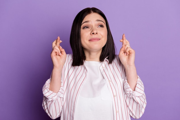 Photo of young pretty woman crossed fingers look empty space pray hope luck isolated over violet color background