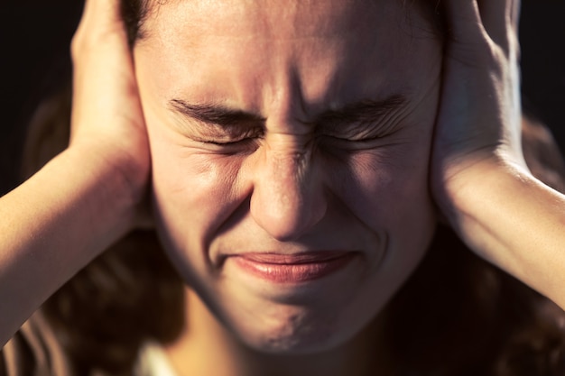 Photo of a young woman close-up with headache on black background. Mental illness concept.