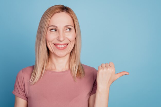 Photo of young woman happy positive smile look indicate thumb empty space ad promo advice isolated over blue color background