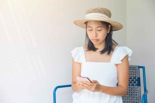 Photo of young woman happy in a white dress and straw hat positive smile use smartphone Concept of social technology travel rest