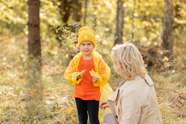 Photo of young woman mom is walking in autumn park with daughter little girl, playing and have together fun with autumn yellow leaves