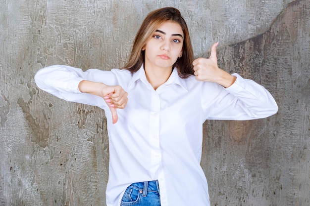 Photo of young woman in white blouse standing and giving thumbs up. High quality photo