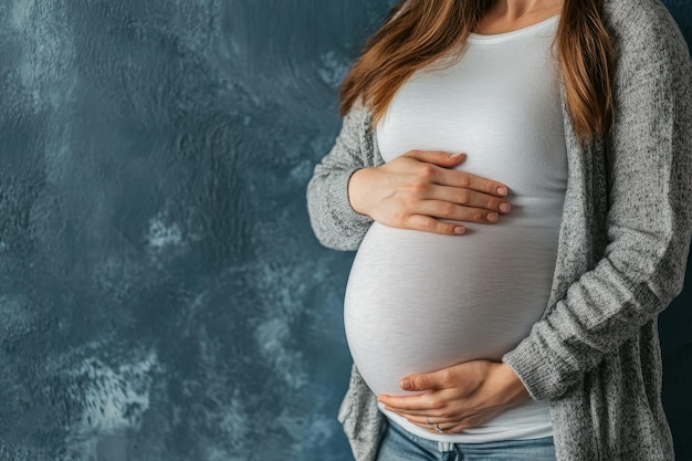 Photo photograph of an unrecognisable woman during the last months of pregnancy holding a big belly gently against a blue wall