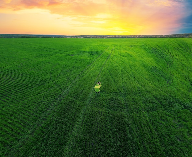 Photographer in a green field with a camera on a tripod photographs the sunset