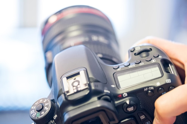 Photographer holds a reflex camera with telephoto lens in his hand Table and laptop in the blurry background