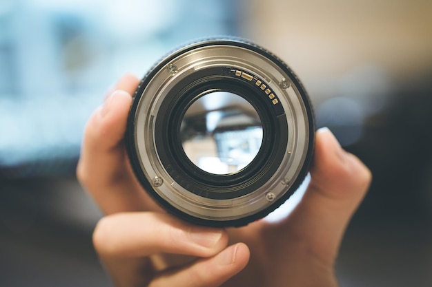 Photographer is holding a photography lens in his hand laptop in the blurry background