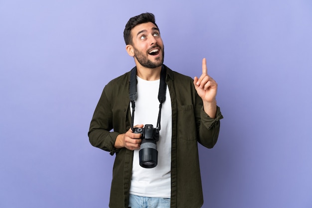 Photographer man over isolated purple wall pointing up and surprised