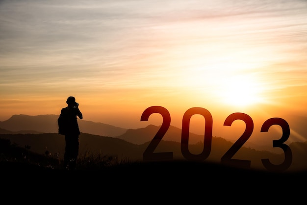 Photographer man standing on the mountain and photo shoot happy new year 2023 concept silhouette of success with beautiful sunset background Happy New Year 2023 for web banner and advertisement