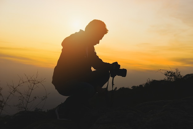 photographer man with a camera on the top of the mountain with sunset sky