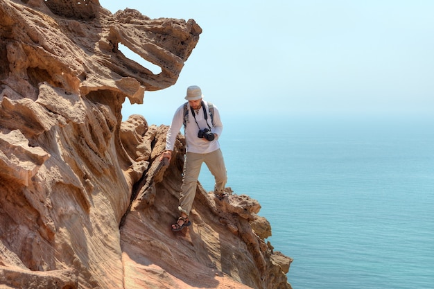 Photographer traveler climbs cliff above sea, Hormuz Island, Hormozgan, Iran.