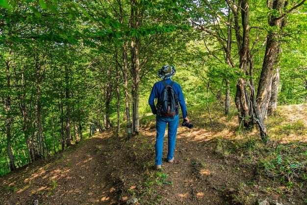 Photographer traveler with a backpack walks in forest along the path