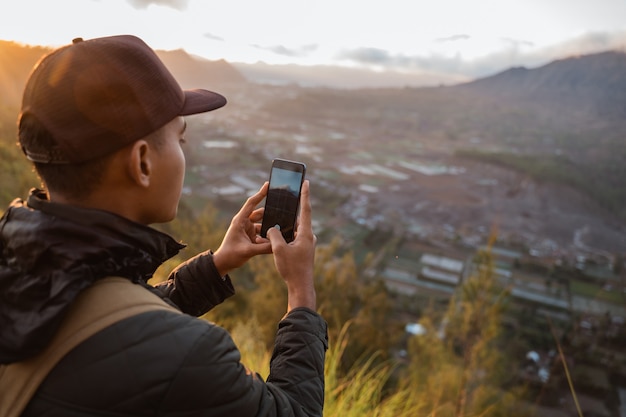 Photographer with backpack and phone taking photo of mountains