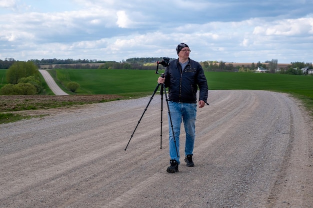 Photo photographer with photographic equipment and tripod on a dirt road