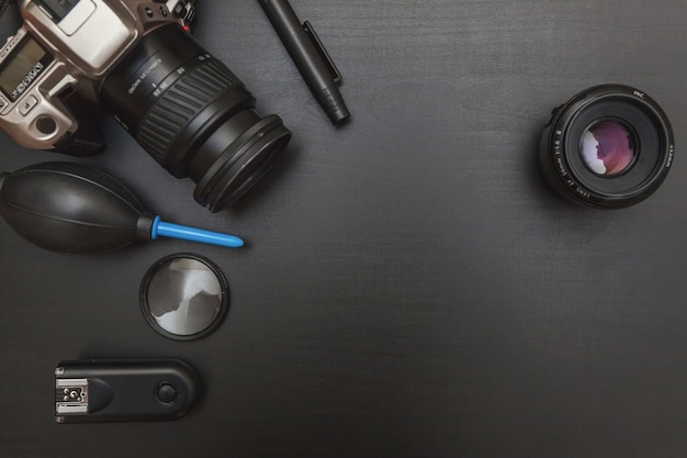 Photographer work place with dslr camera system, camera cleaning kit, lens and camera accessory on dark black table background