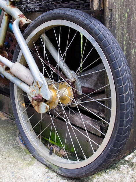 A photography of a bike with a rusted tire parked in front of a building