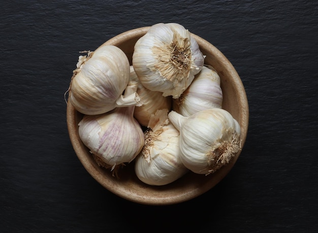 Photography of garlic heads in a wooden bowl on slate background